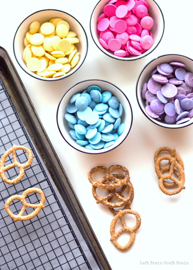 candy melts in yellow, pink, purple, and blue and pretzels on wire rack