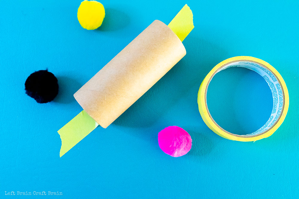 tape toilet paper roll to table with pom poms