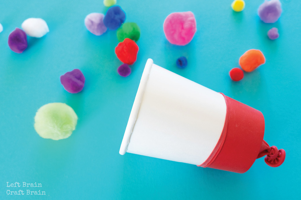paper cup with balloon on it with pom poms on blue