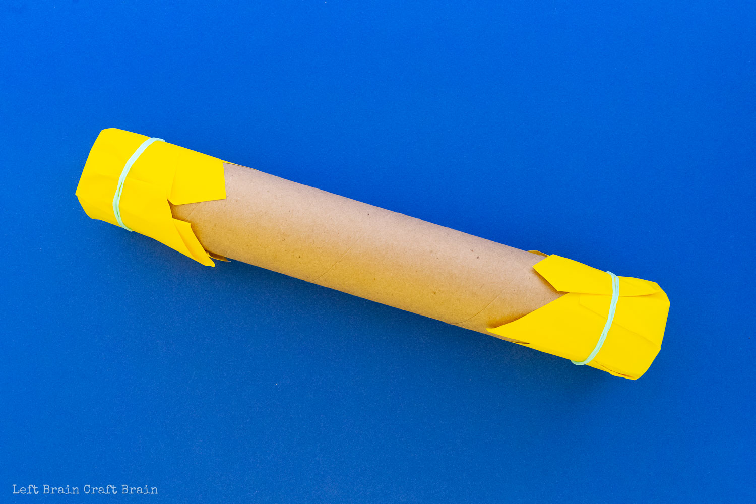 paper towel roll rain stick with paper and rubber bands on blue