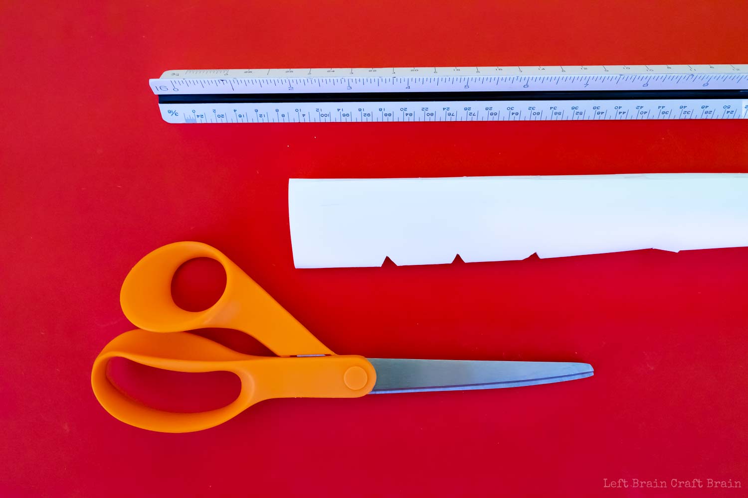 paper flute with triangle keys cut out, orange scissors, and ruler on red background