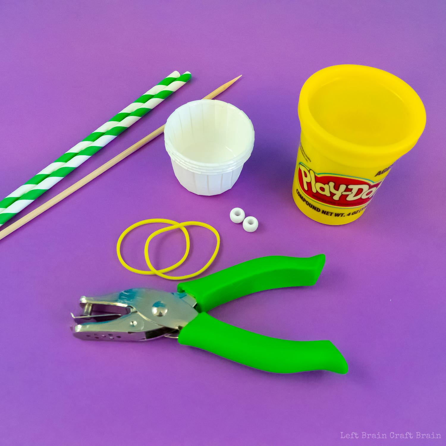 supplies to make paper cup anemometer on purple background (paper straws, bamboo skewer, pony beads, hole punch, rubber bands, paper condiment cups, and playdoh cup)