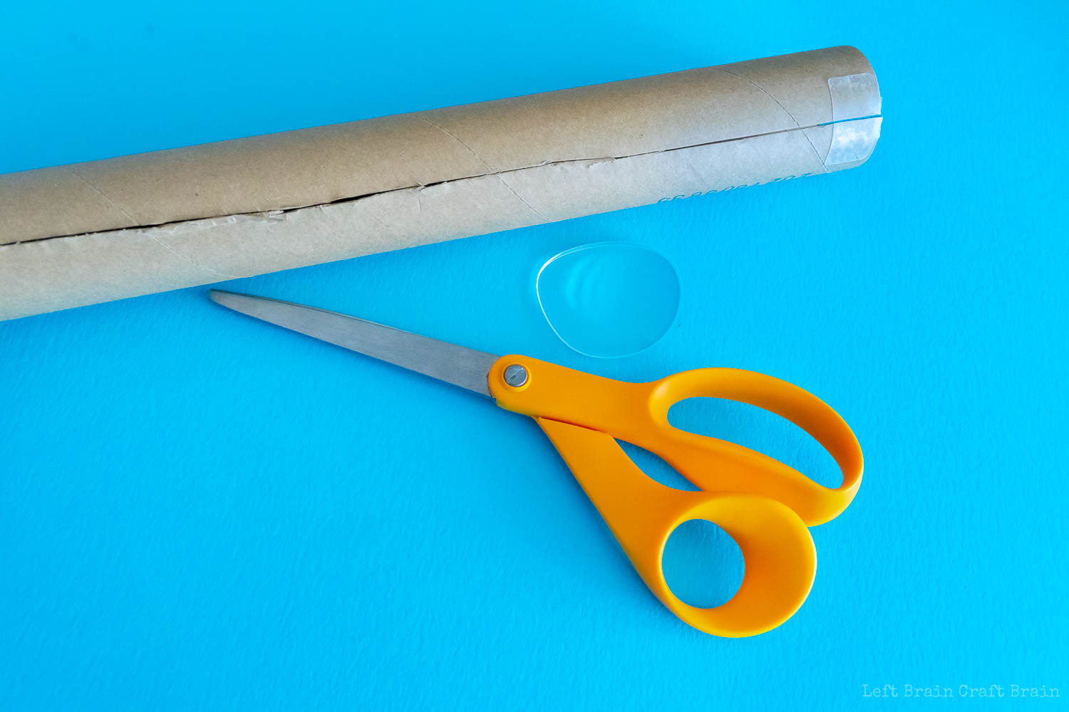 how to make a telescope - paper towel roll with a slit down the side with eyeglass lens and orange handles scissors sitting underneath on blue paper